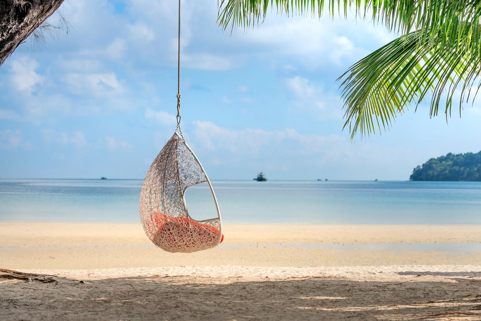 Een hangstoel aan een touw op een zonnig strand onder palmbladeren